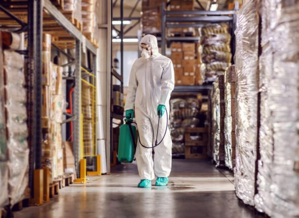 Man in protective suit and mask disinfecting warehouse full of food products from corona virus / covid-19.
